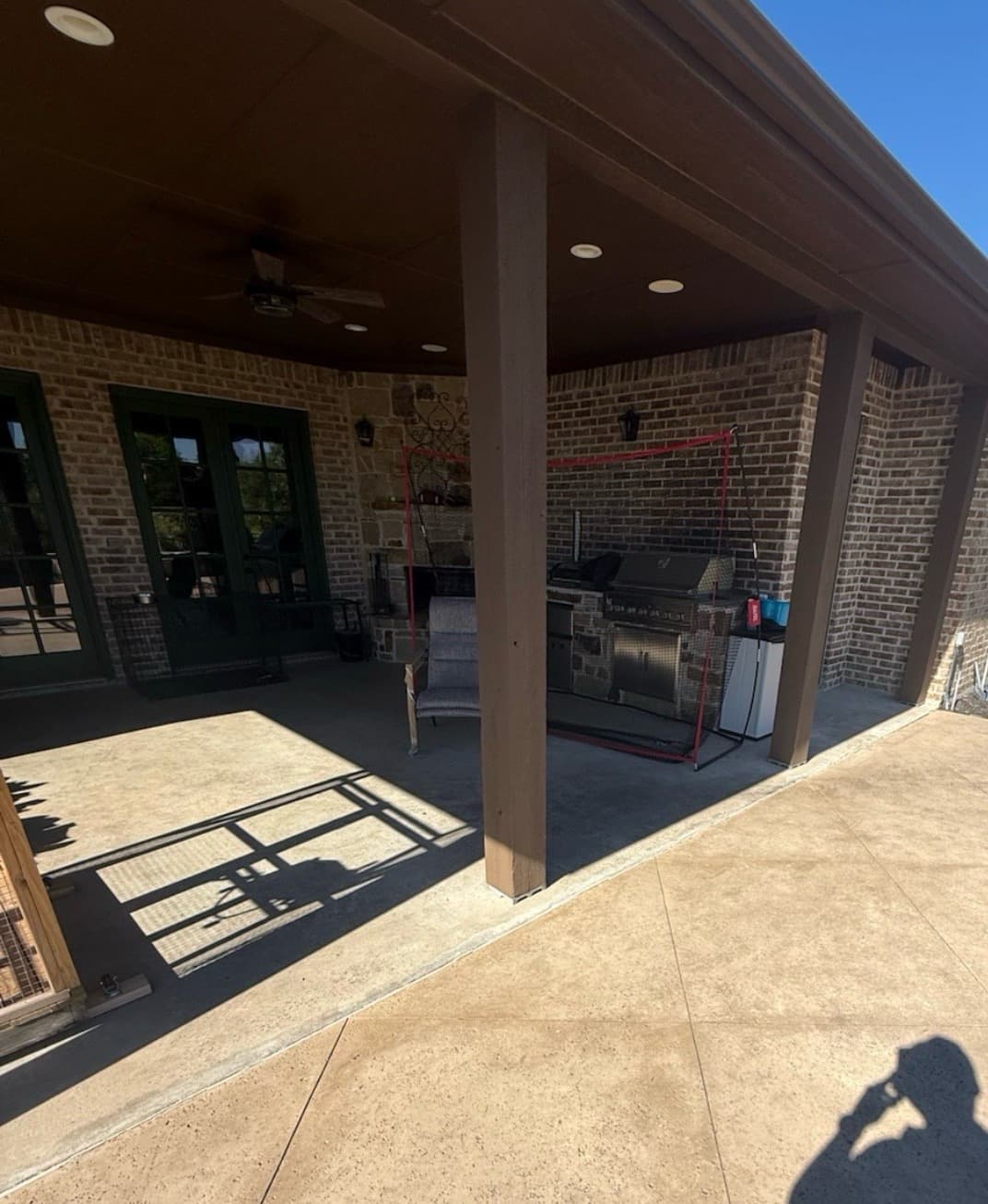 Covered patio before renovation — bare concrete slab, original brick columns, and dated furniture under a brown-painted ceiling.